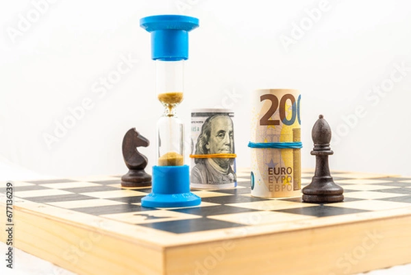 Obraz Chess board with black bishop and black knight, rolled euro and dollar bank notes and an hourglass. Concept of business strategy, leadership