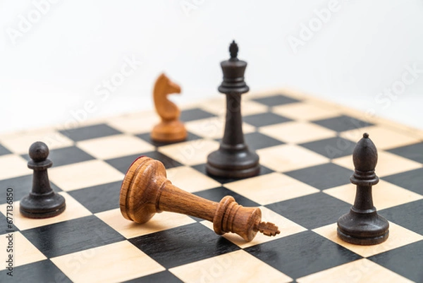 Obraz Angle view on chess game with black and white pieces. White king defeated, black pawn, bishop and king standing