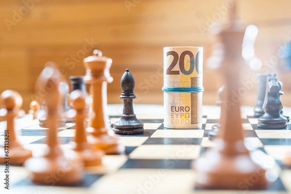 Obraz Chess board with blurred black and white chess pieces playing against euro bank notes.