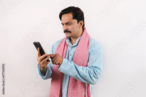 Obraz portrait of disappointed, sad Indian farmer man in rural India concept. white background. Cheerful farmer looking into the mobile phone screen, using advanced technology.