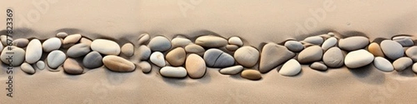 Fototapeta Panoramic view of a line of stones embedded in the sandy shoreline, creating a tranquil and visually captivating scene.