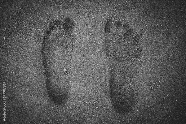 Obraz Black and white human barefoot footprints in wet, black volcanic sand of a beach. 