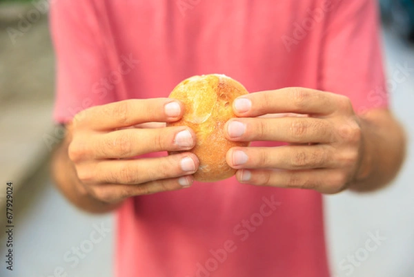 Fototapeta A man's hand holds a round bun, snack and fast food concept. Selective focus on hands with blurred background