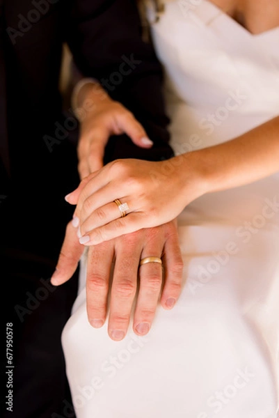 Obraz Bride and groom are sitting together with their hands together showing off their wedding bands. 
