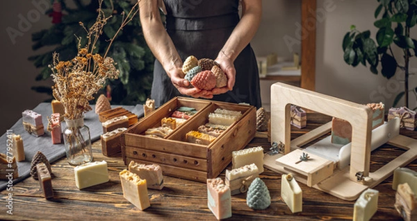 Obraz A woman soap maker holds soap in her hands in the form of colorful coniferous cones. An interesting gift for New Year's holidays and Christmas. Eco-friendly natural handmade cosmetics