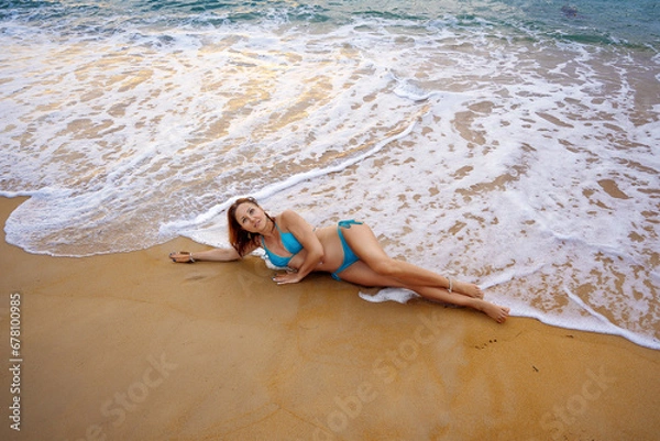 Fototapeta A beautiful girl in a bikini on a wild beach, bathing in the clear waves of the warm sea. a heavenly place and a beautiful model.