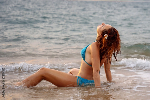 Fototapeta A beautiful girl in a bikini on a wild beach, bathing in the clear waves of the warm sea. a heavenly place and a beautiful model.