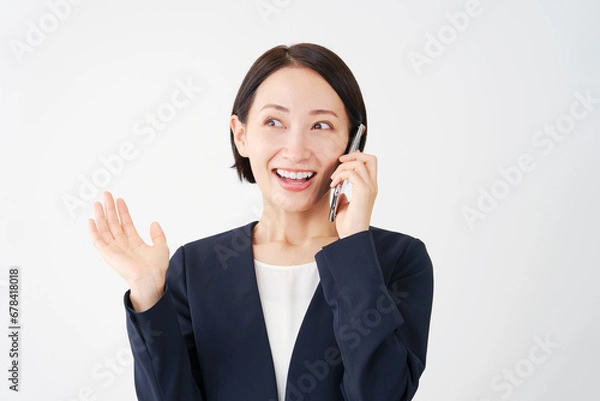 Fototapeta スマートフォンで電話をしながら笑顔で驚く中年のビジネスウーマン　白背景