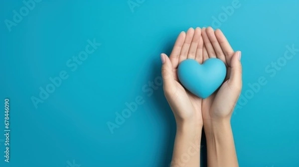 Fototapeta A blue heart held by two hands on a blue background, representing affection and compassion