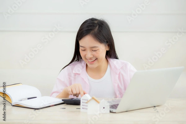 Fototapeta Young asian woman sitting and planning and calculate expense and mortgage with calculator and home on desk, insurance and budget of residential, loan and residence, business and property concept.