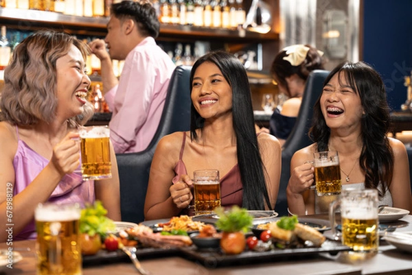 Fototapeta Beautiful Asian woman is Relishing a Delightful Dinner with Friends at a Bar, Immersed in the Joy of a Vibrant Night Party. They Enjoying with Night Party Together. Party and Celebration Concept.
