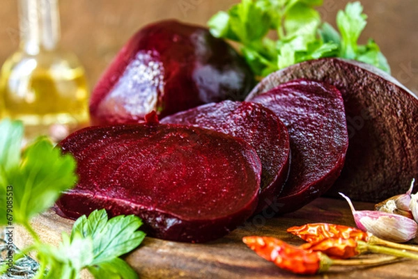 Fototapeta Sliced boiled beets on a dark wooden background. Slices of boiled red beetroot, garlic, red hot pepper and parsley lie on a wooden table.