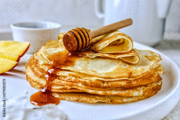 Fototapeta A stack of pancakes with honey on a white ceramic plate. Pancakes with honey and nectarines on a light background. Pancakes on a white plate, selective focus. Russian traditions. Russian holiday. Masl
