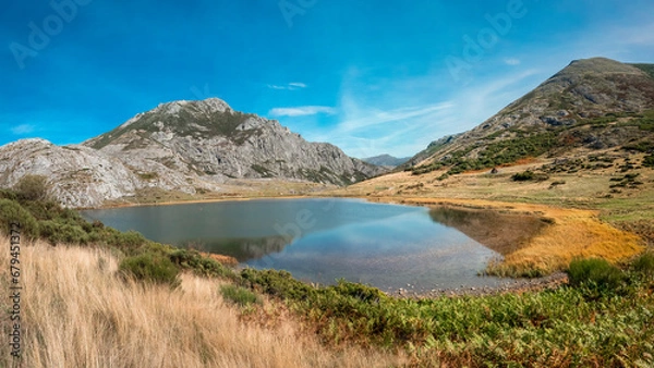 Fototapeta Lake of glacial origin on a sunny day with blue skies, situated between meadows and mountains in the north of León, Spain.