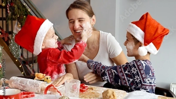 Fototapeta Two cheerful boys playing with mother and throwing flour in her while cooking on kitchen on Christmas