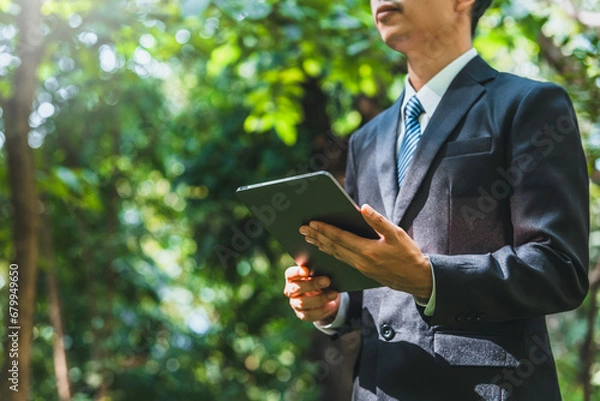 Fototapeta Business man using tablet to analyze Renewable energy generation is essential for the future. Renewable energy-based green business can limit climate change and global warming.