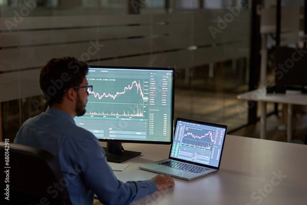 Obraz Busy business man trader broker analyst investor using laptop computer analyzing stock exchange trade crypto digital data investing finances in stock market platform working in dark night office.