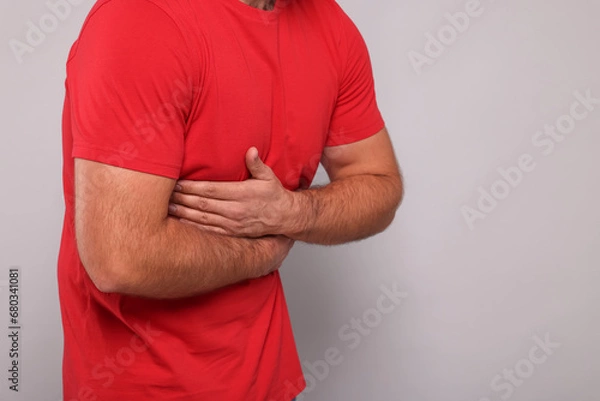 Fototapeta Man suffering from stomach pain on grey background, closeup. Space for text