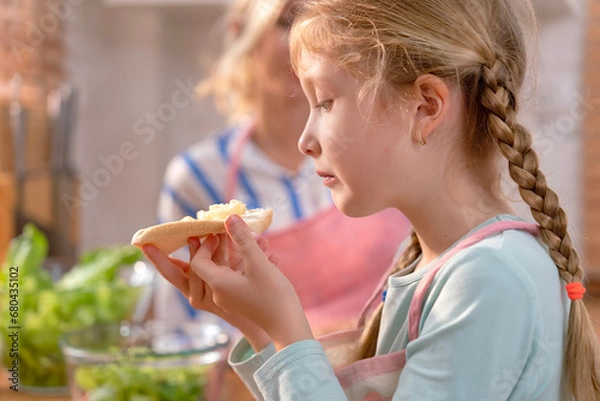 Fototapeta Selective focus, A cute girl feeling hungry cooked a simple sandwich of bread and banana while waiting for her mother cooking the main dish finished in the kitchen.