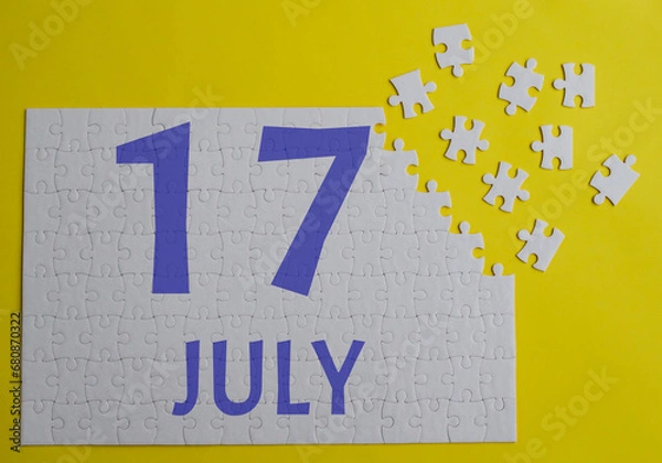 Obraz 17 july calendar date on a white puzzle with separate details. Puzzle on a yellow background with a blue inscription