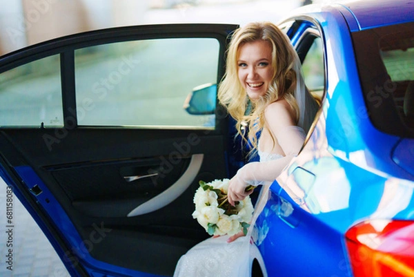 Fototapeta a beautiful and happy bride with a bouquet in a blue car