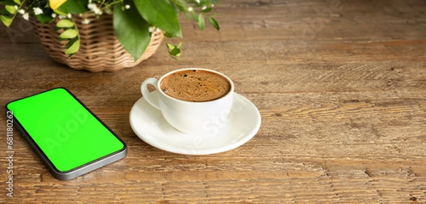 Fototapeta Cup of hot coffee and smartphone with green screen on rustic wooden background. copy space