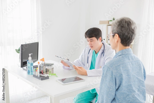 Fototapeta asian doctor talk with old patient in hospital, he screening and write patient information on patient chart, elderly healthcare promotion