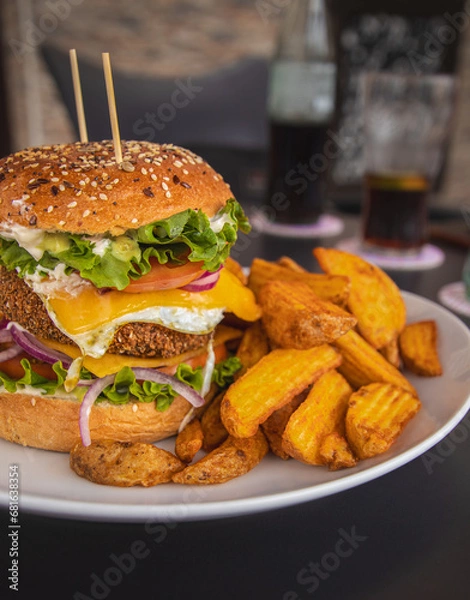 Fototapeta Crispy chickpea veggie burger, served with deluxe potatoes, egg, lettuce, cheese, tomato, onion. With the drink in the background. Delicious vegetarian meal.