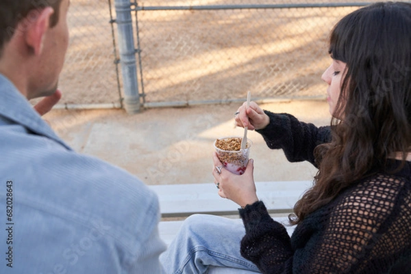 Obraz Couple eats yogurt and protein bar on bleachers outside