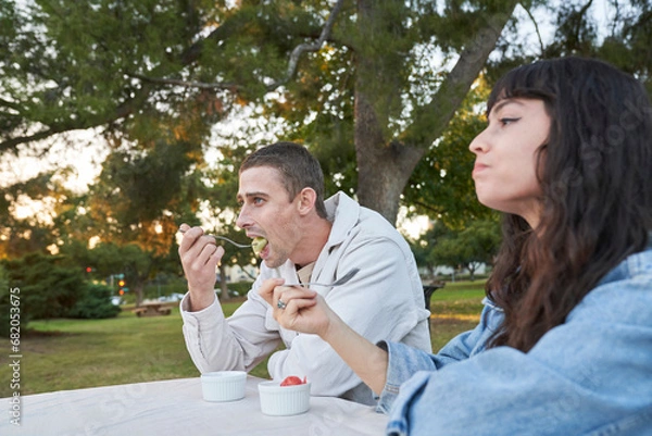 Obraz Couple eats fruit salad at picnic table in park