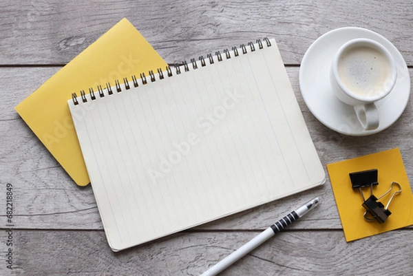 Fototapeta Blank notepad on yellow notepad and cup of coffee on wooden table in office