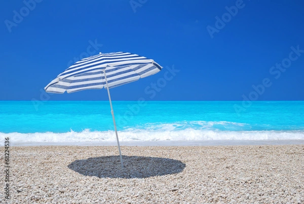 Fototapeta Sun umbrella on a pebble beach with turquoise sea and sky