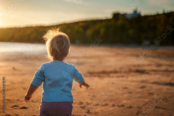 Fototapeta Little baby child toddler walks along an empty beach by the sea at sunset alone, calm and relax, active childhood
