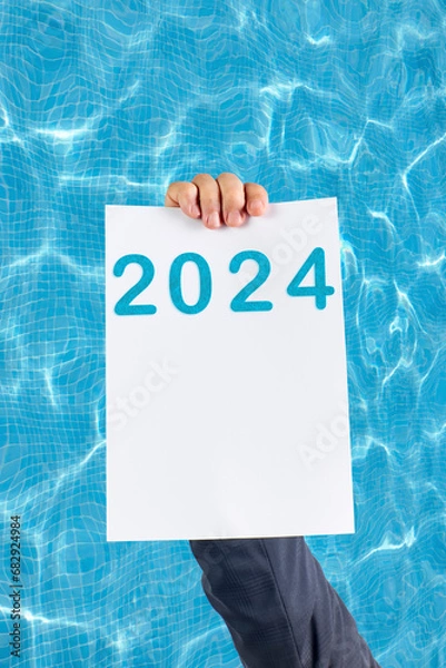 Fototapeta 2024, Man holding cardboard with number 2024 on background of faded lights. Happy New Year