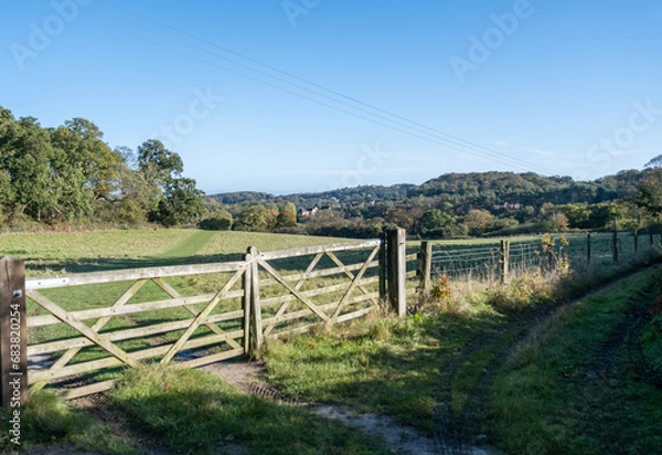 Fototapeta Wooden gate across a grassy meadow in the countryside. Captured on a bright and sunny morning
