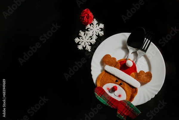 Fototapeta Preparation for the festive feast: transformation of the Christmas table. Top view photo of plate, cutlery, napkin, snowflake, red layer isolated on black background. Copy space for text