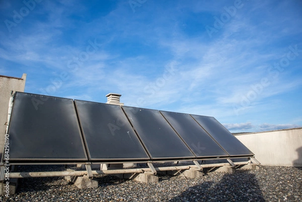 Obraz solar panels, five solar panels on the roof of a residential building, in the background you can see the blue sky and some clouds