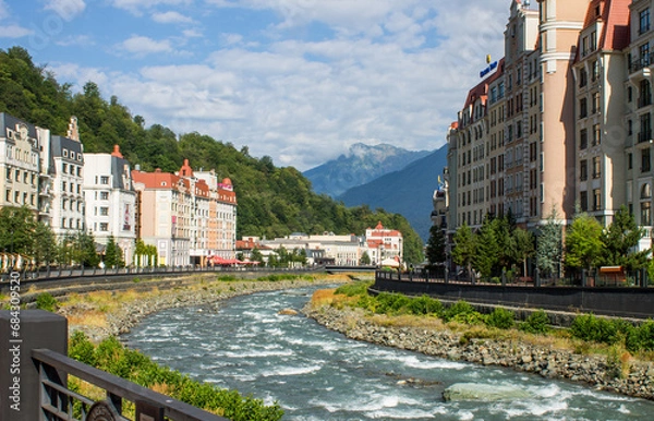 Obraz Krasnaya polyana, Krasnodar Krai, Russia - July, 29, 2023: the embankment of the Mzymta River and modern architecture with luxury apartments among green hills on Krasnaya Polyana on a sunny summer day
