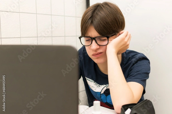 Fototapeta A tired student with a laptop is doing homework, preparing for exams.