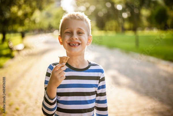 Fototapeta Portrait of happy boy who is standing in park and eating ice cream.