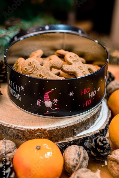 Obraz Christmas box with gingerbread men, complemented by natural decorations walnuts, pine cones, oranges evoking warm holiday ambiance, rustic charm, one gingerbread man holding another one's hand.