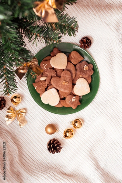Fototapeta Gingerbreads, line cakes arranged on a green plate beneath the Christmas tree capturing a bird's-eye view of festive sweetness. The warm, spicy aroma of gingerbread mingles with the evergreen scent.
