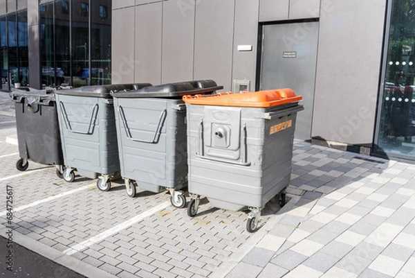 Fototapeta Row of worn out recycing and waste bins in a car park at the back of a modern office building
