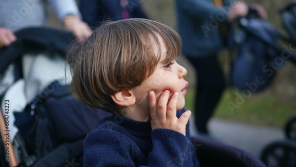 Obraz Pensive child thinking while seated on stroller with hand in chin. Young boy observing world with thoughtful expression while being carried in carriage