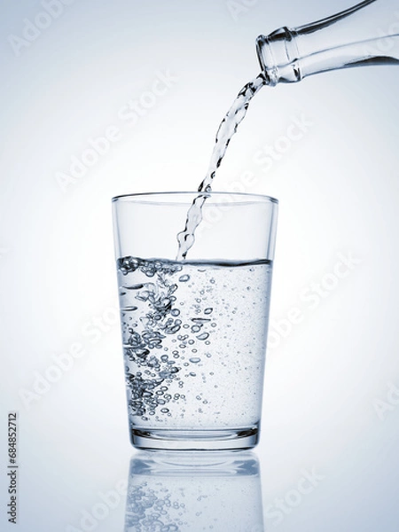 Fototapeta Water pouring from a bottle in a glass with bubbles on blue background