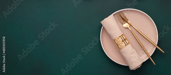Fototapeta Plate with fork and knife. Mockup with empty space. Gold cutlery, dark green background. Top view. Celebration place setting, fabric napkin. Dining table in restaurant. Menu template, flat lay, banner