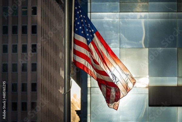 Fototapeta American flag waving in the wind on the pole in front of large windows and buildings of Lower Manhattan, New York City