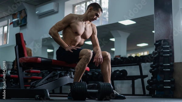 Fototapeta Muscular shirtless man sitting on a bench and resting after a workout. 