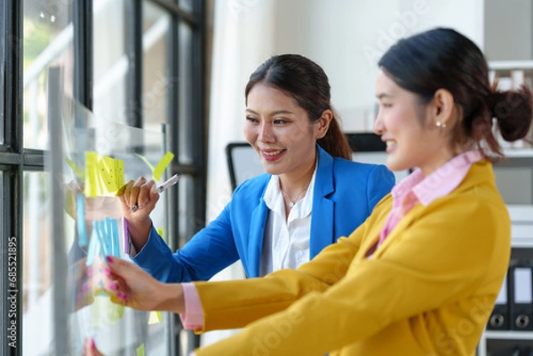 Fototapeta A group of young business people plan and brainstorm together to record. Place sticky notes on the glass wall in your financial business to ensure success according to company policies in the office.
