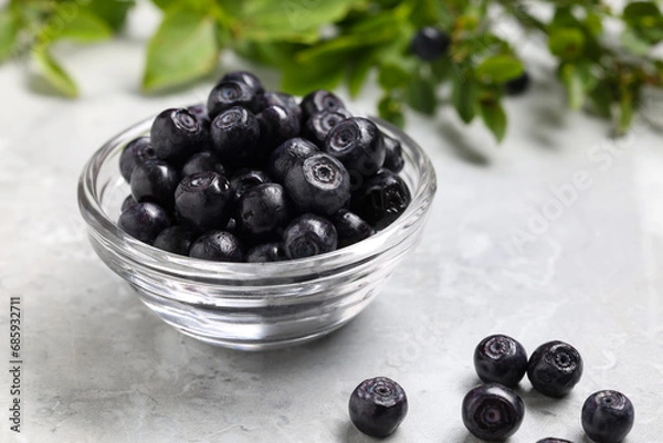Fototapeta Ripe bilberries in bowl on light marble table, closeup